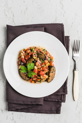 Summer salad of eggplant and tomato on a white plate on a light background