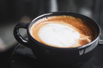 close up modern hot black coffee the cappuccino on dark background with coffee bubble foam pattern and texture in black cup looking and feel so delicious on glasses table in coffee shop.