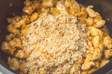 Laying wild rice and chicken pieces for making pilaf in slow cooker.