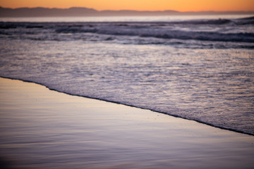 Water rushing into shoreline with sunrise in the background