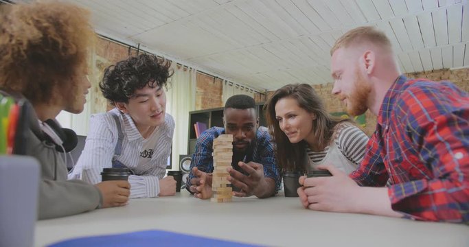 Multiracial colleagues play in board games, black guy accurately takes one block out of tower