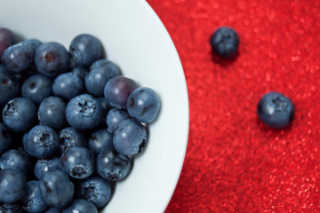 Fresh blueberries in a white bowl on red glittering background.
