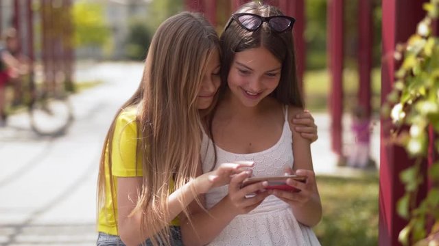 Two young teenage girls excitedly play on a smartphone app