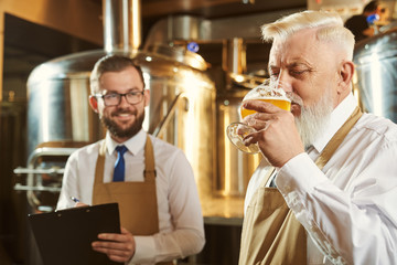 Bearded brewer keeping glass of beer and drinking beverage