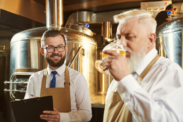 Happy young brewer keeping folder and looking at colleague