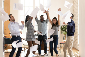 Overjoyed multiracial business team people tossing papers dancing in office