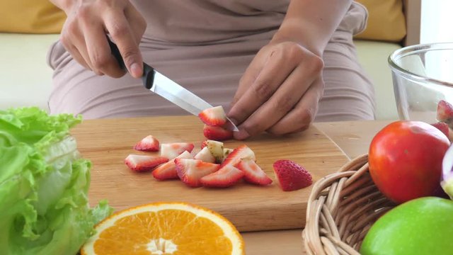 Closeup of woman slicing red strawberries with vegetable and fruits for making healthy salad. Food cooking and ingredients. Ketogenic diet food concept. People lifestyle and leisure.