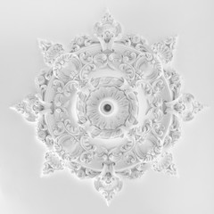 Decorative item made of white plaster on ceiling and wall. Beautiful ornament and relief stucco interior