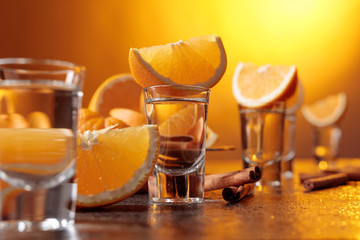 Glasses of gold tequila with orange and cinnamon sticks.
