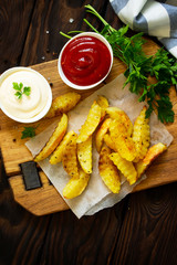 Homemade Tasty french fries on cutting board with Mayonnaise and with ketchup, on wooden table background. Top view. Space for text.