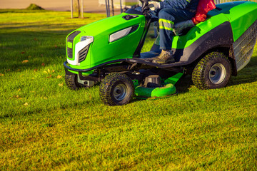 Gardener worker on lawn mower tractor cuts green grass