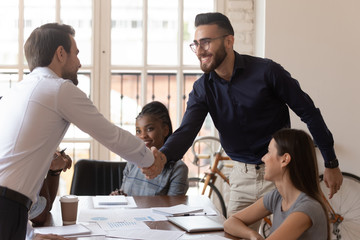 Two happy businessmen shake hands at group negotiation greeting