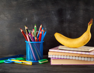 yellow banana on a stack of notebooks, a blue stationery glass with multi-colored wooden pencils