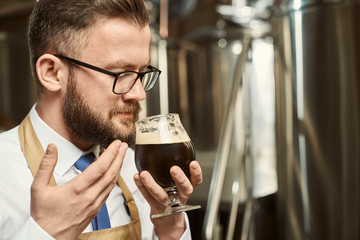 Closeup of bearded man in glasses smelling tasty dark beer