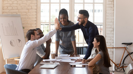 Motivated male colleagues give high five at multiracial group meeting