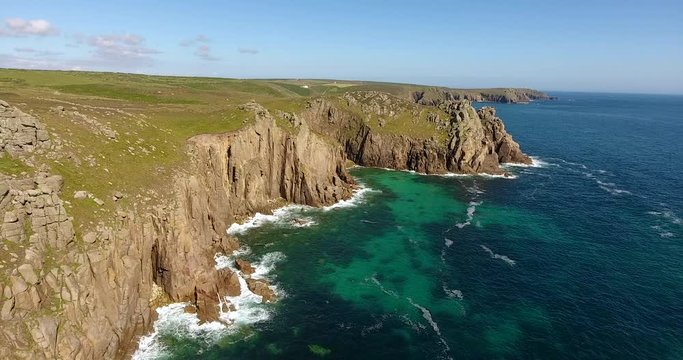 Flying along dramatic rocky rugged cliffs, turquoise sea waters, summer landscape in Cornwall, south west England. 
