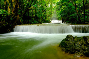 Multi-layered water fall with one rock in front of it in the forest of national park, Thailand.