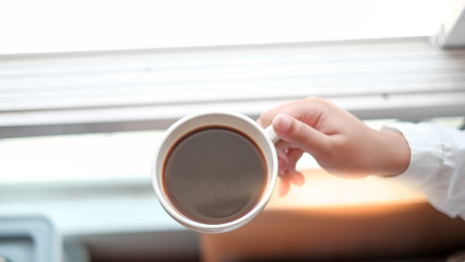 Women wear white long hair, 20 years old, using both hands to catch a cup of coffee in the morning. out of  focus.