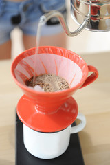 Girl barista brews coffee drip method. Pouring water from gooseneck kettle into red hario v60 funnel.