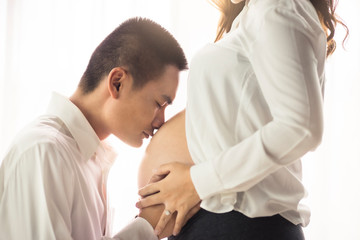 Close up Asian man husband kiss pregnant wife at home. Pregnancy and family concept.