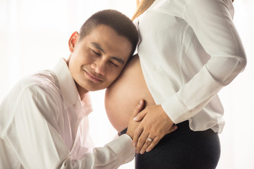Close up Asian man husband hugging listen belly pregnant wife at home. Pregnancy and family concept.