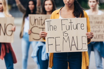 cropped view of girl holding placard with inscription the future is female near feminists on street