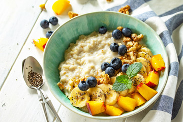 Healthy food for Breakfast, vegetarian, vegan, alkiline diet food concept. Oatmeal porridge with chia, banana and blueberry on fruits and nuts on a white wooden table.