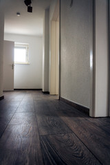 Blick in einen leeren Flur mit abgehenden Zimmern und hellem Fenster das Echtholz Parkett bestrahlt