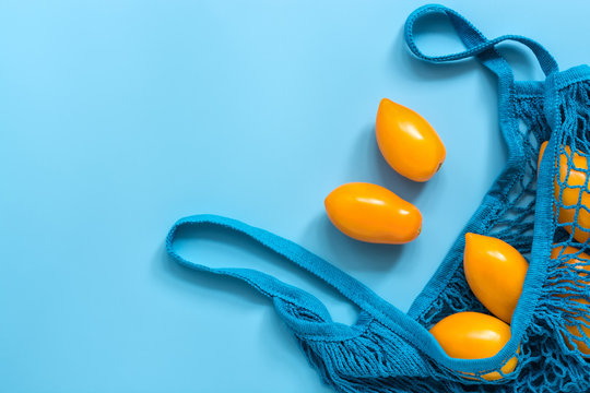 Fresh yellow tomatoes in a cotton string bag on a blue background. Flat lay, top view, copy space