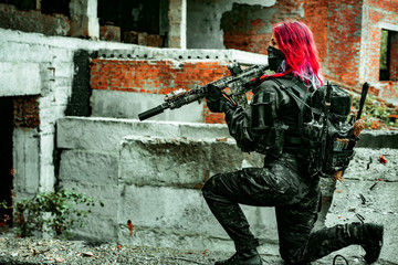 Fototapeta premium Airsoft red-hair woman in uniform with machine gun standing on knee. Soldier on ruine. side view