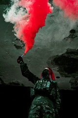Fototapeta na wymiar Airsoft red-hair woman in uniform with red smoke in hand. Close up soldier in broken building.