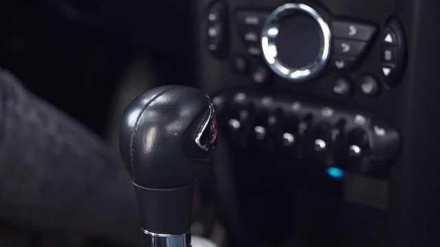 Close-up of female driver hand switching automatic transmission in luxury car before driving. Black car interior view, woman sitting on driver's seat shifting gear knob going to drive car