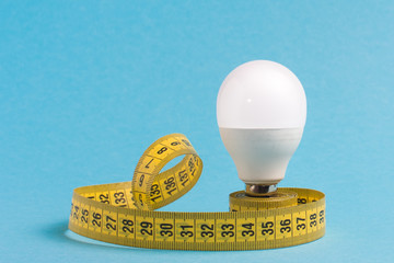 Measuring tape wrapped around a light bulb on a blue background. Minimum creative concept, the...