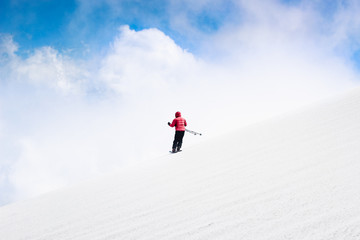 Naklejka na ściany i meble Skier skiing downhill slope in red jacket. Sky and clouds behind horizon. Freeride skiing. Alpine sports, white snow. Minimalist photography. Danger, action speed concept