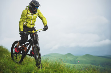 Front view of a man on a mountain bike standing on a rocky terrain and looking down against a gray sky. The concept of a mountain bike and mtb downhill
