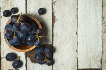 Dark grapes inside a wooden bowl, on a white wooden table.