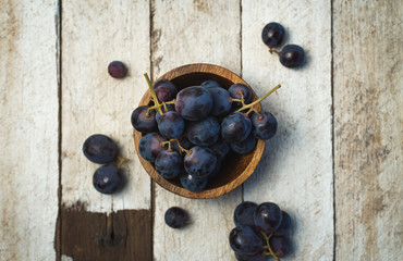 Dark grapes inside a wooden bowl, on a white wooden table.