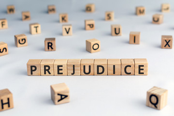 prejudice - word from wooden blocks with letters,  personal opinions prejudice bias concept, random letters around, white  background