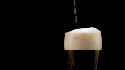 dark Beer is pouring into glass on black background. - Powered by Adobe