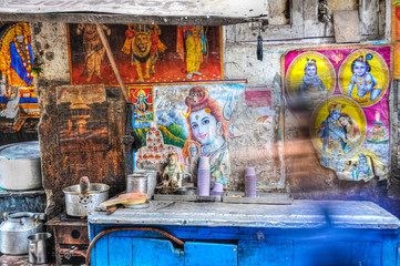 Chai tea street food stall with posters of shiva the god on the wall and a blurry person walking by in Delhi India