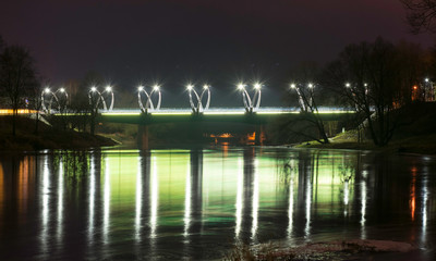 Fototapeta premium mysterious night landscape overlooking illuminated bridge, fuzzy and misty outline, evening light, haze, Valmiera, Latvia