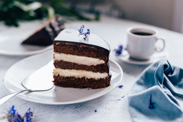 Chocolate cake on a plate and a cup of coffee and lilac flowers for decor on the table