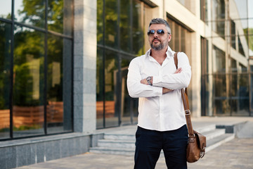 Middle-aged bearded handsome business man in sunglasses and white shirt used mobile phone on the office building background