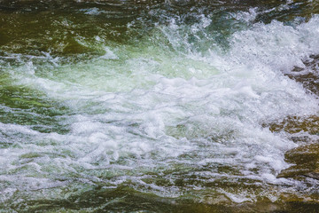 Waves in the mountain river. Fast flow of water_
