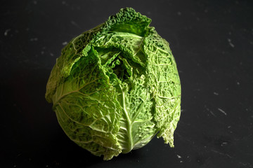 Closeup of savoy cole cabbage on black desk with marble effect. - obrazy, fototapety, plakaty