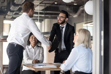 Smiling businessmen partners shaking hand, making agreement at meeting