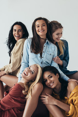 front view of five smiling attractive multiethnic feminists in colorful shirts embracing and looking at camera isolated on grey