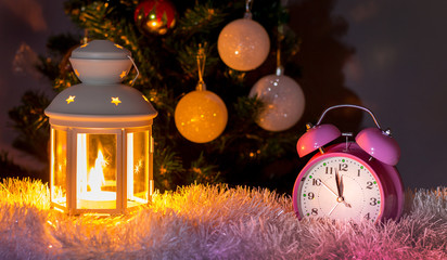 Clock and lantern with candle near Christmas tree at midnight. New Year's Eve. New Year and Christmas card_