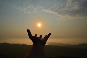 Holding in orange sun with one hand, while there is a beautiful sunset