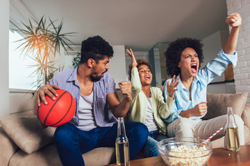 Happy African American family of three watching tv and cheering sport games on sofa at home